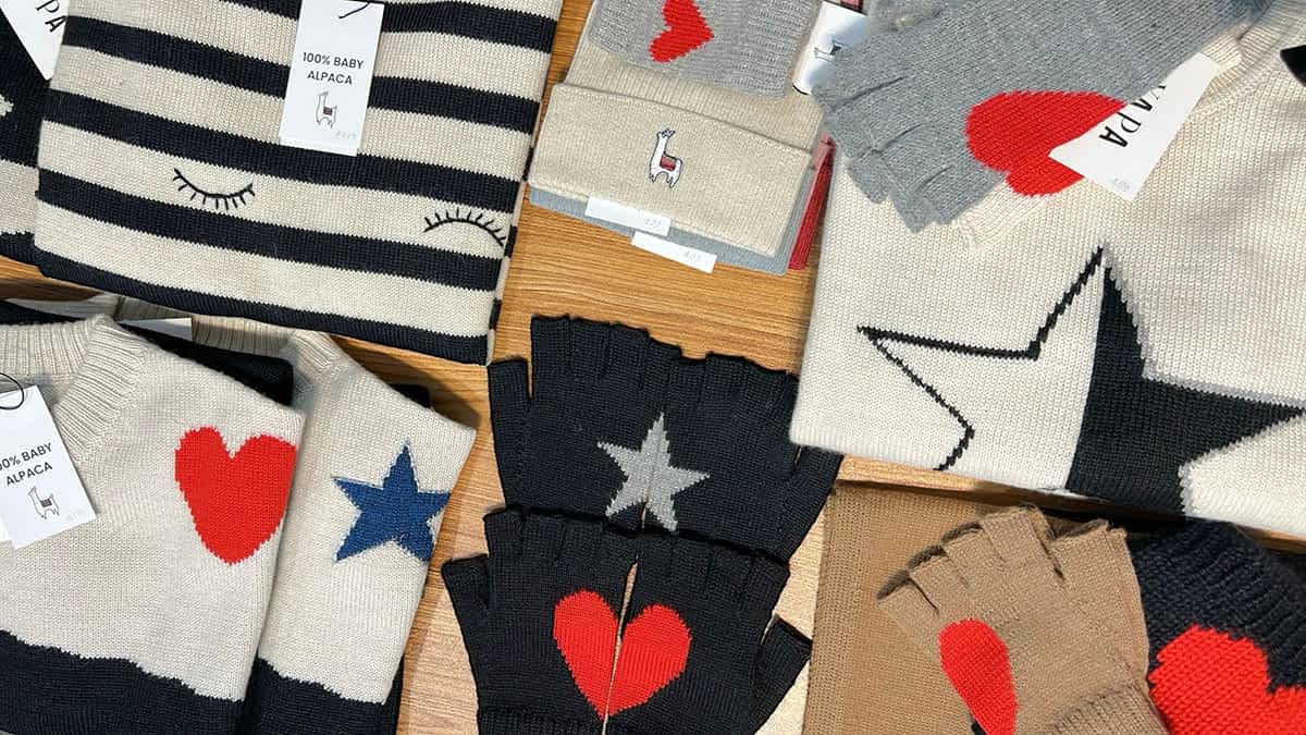 Colorful Yapa alpaca apparel laid out on wood table, sustainable fashion with bold, graphic details